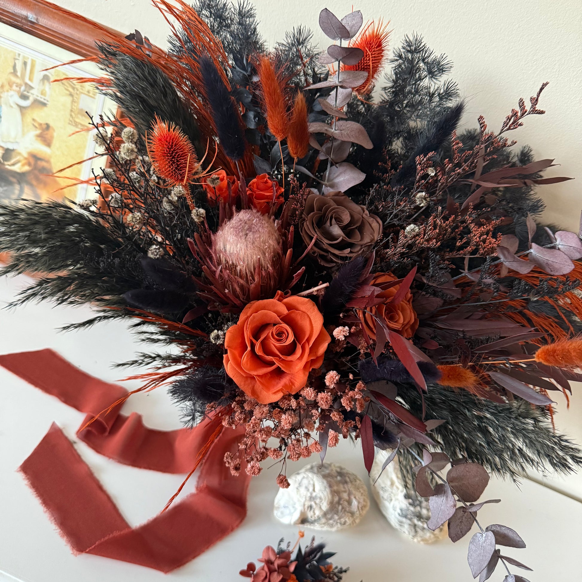 Dried floral arrangement with orange and brown tones on a white surface.