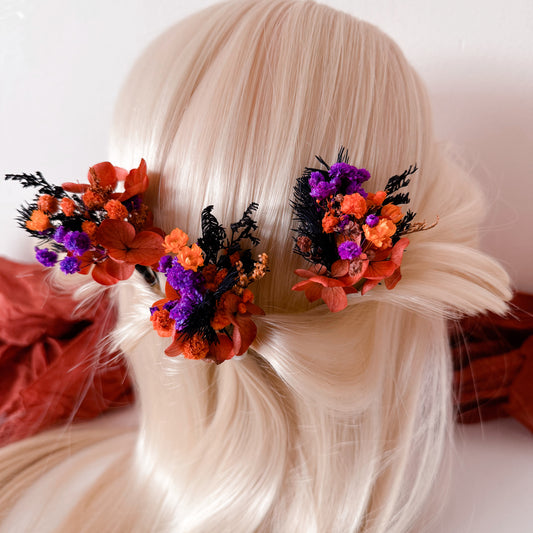 Two dried flower hair pins in burnt orange, purple and black tones placed in a half-up hairstyle on blonde hair — perfect for boho or autumn wedding look.