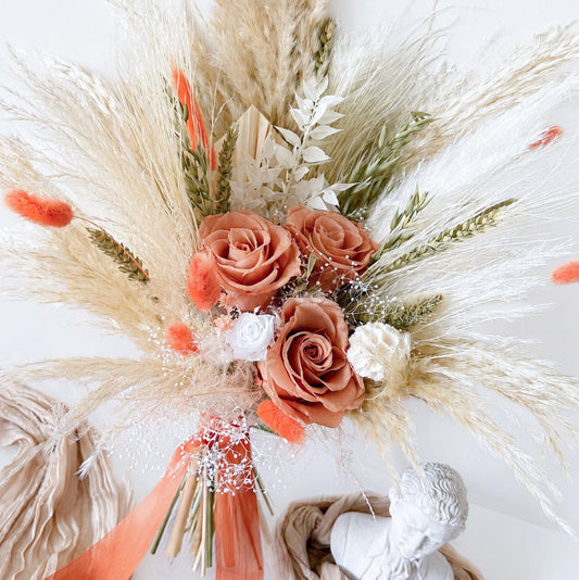 Decorative floral arrangement with coral flowers and pampas grass on a white background