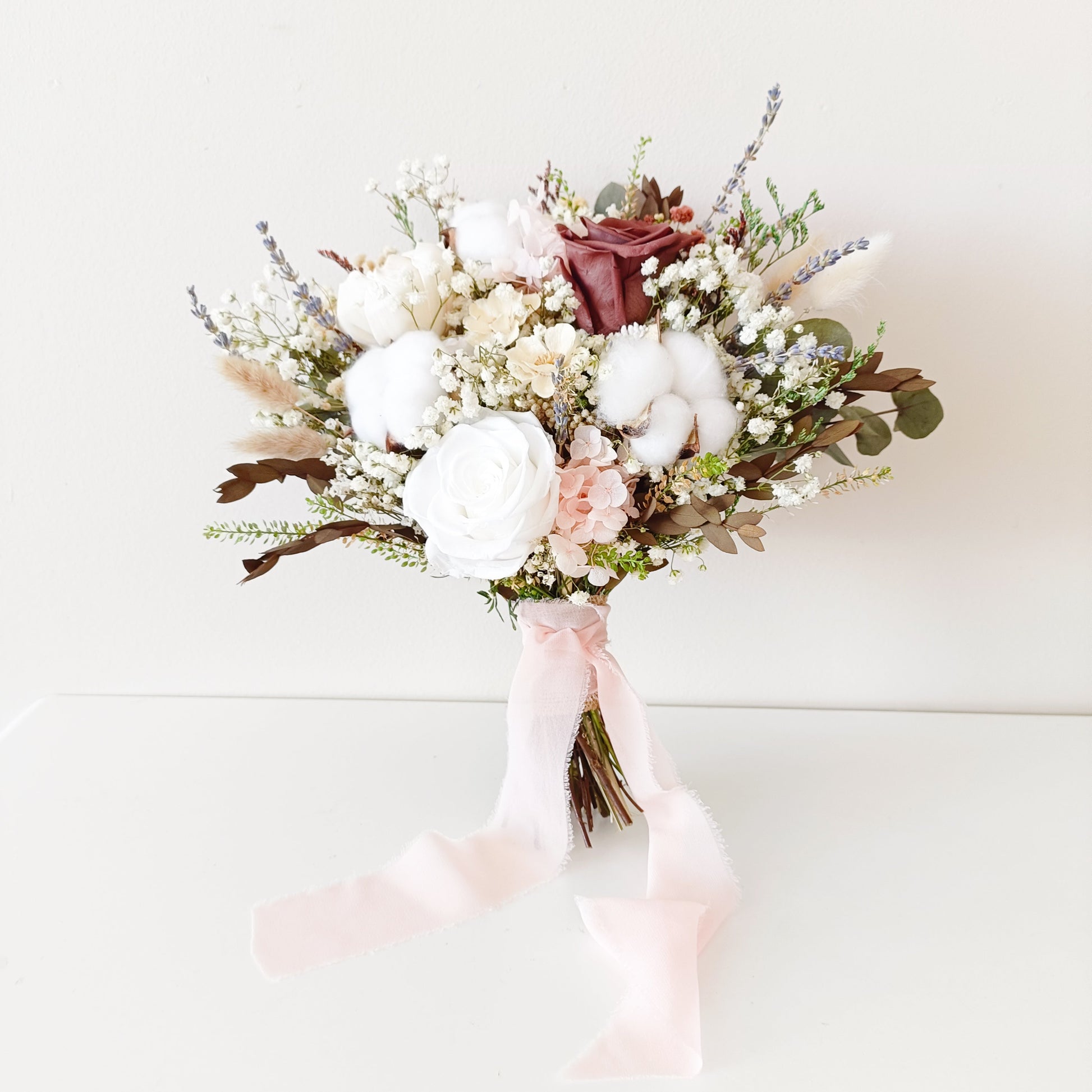 Bridal bouquet in neutral and burgundy tones, styled with pink silk ribbon – preserved cotton, eucalyptus, and sola florals.