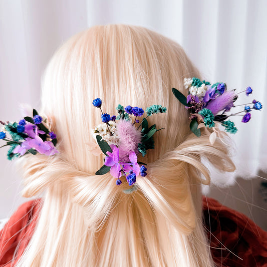 Blonde hair styled with dried  floral hair accessories in purple against a white curtain background