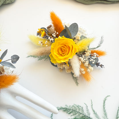 Two dried wrist corsages featuring yellow roses, bunny tails, and orange billy buttons â€” country and boho wedding theme.