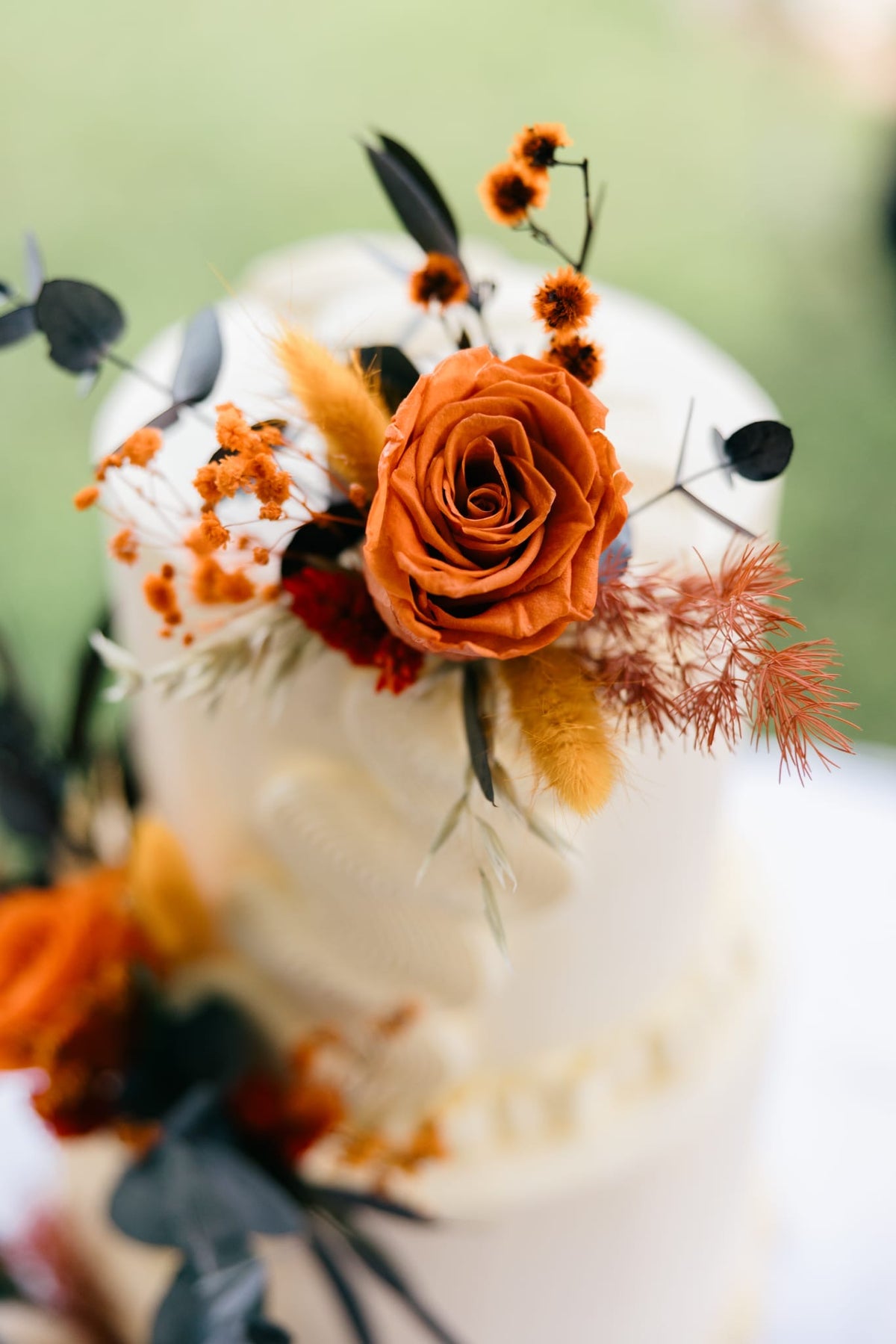 Elegant wedding cake styling with terracotta roses, warm orange blooms and dried foliage in a rustic, modern botanical palette.