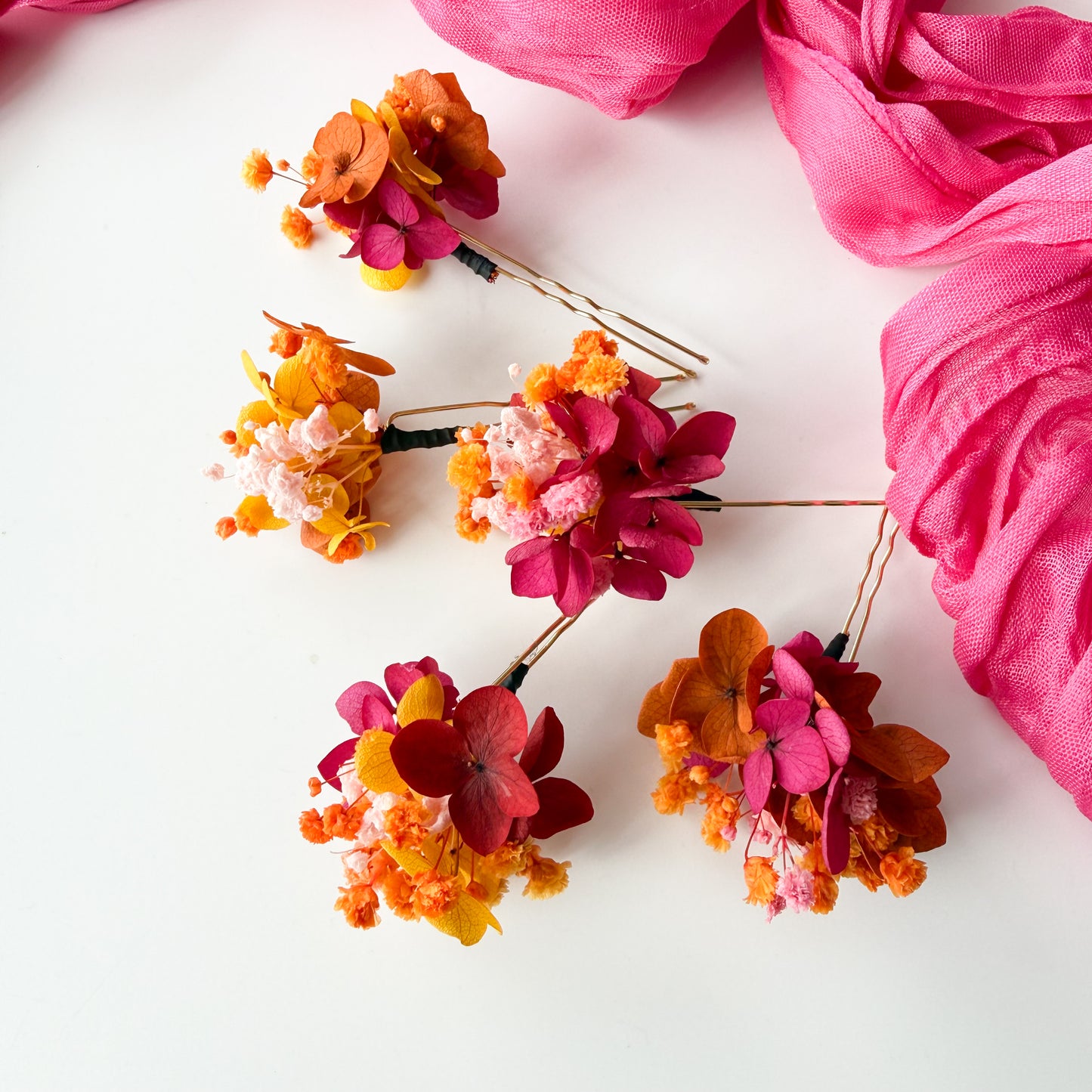 Colorful floral hair accessories on a white background with pink fabric.