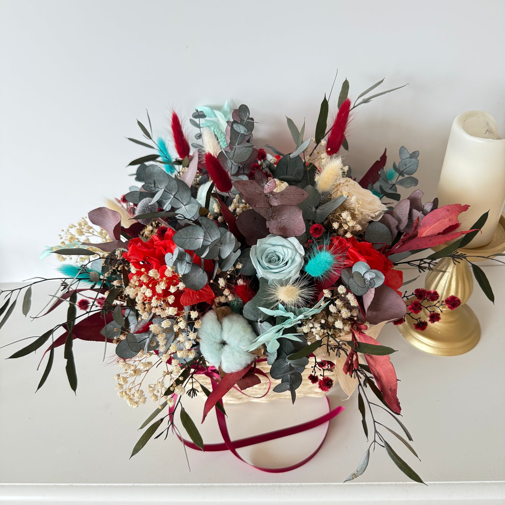 Handmade dried flower centerpiece with Christmas colours, preserved eucalyptus, cotton and bunny tails in a woven basket.