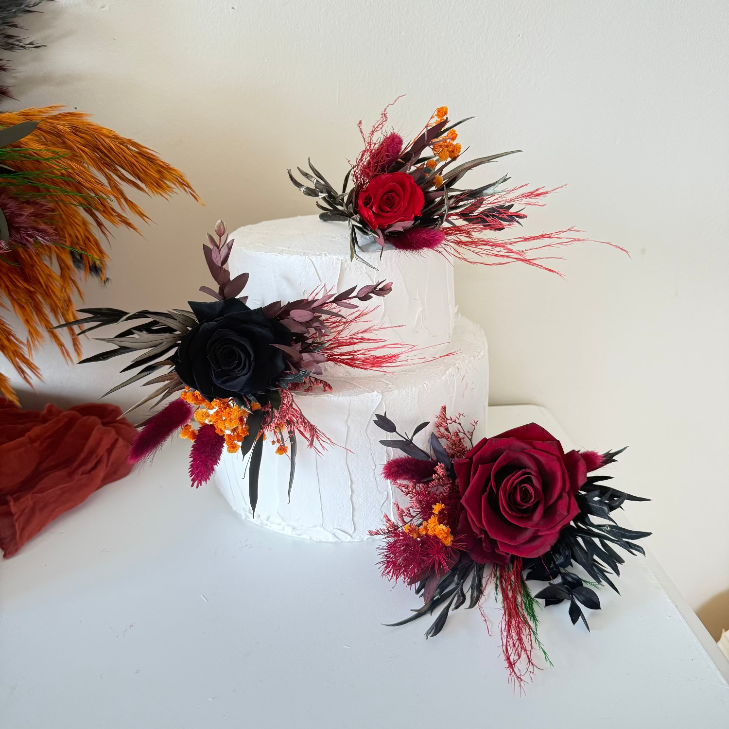 Gothic wedding cake flowers featuring burgundy and black preserved roses, dried flowers and dark foliage, matching a gothic skull wedding bouquet.