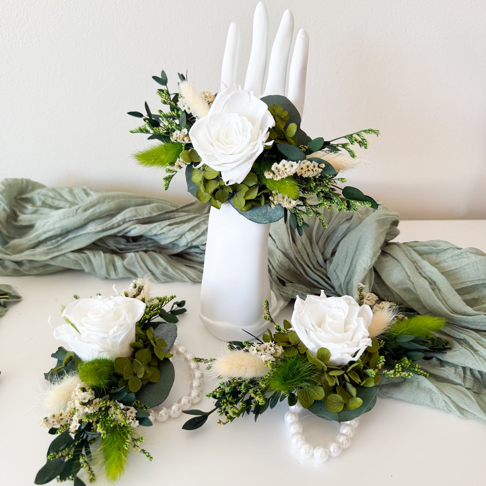 Decorative floral arrangements with white roses and greenery on a white surface.