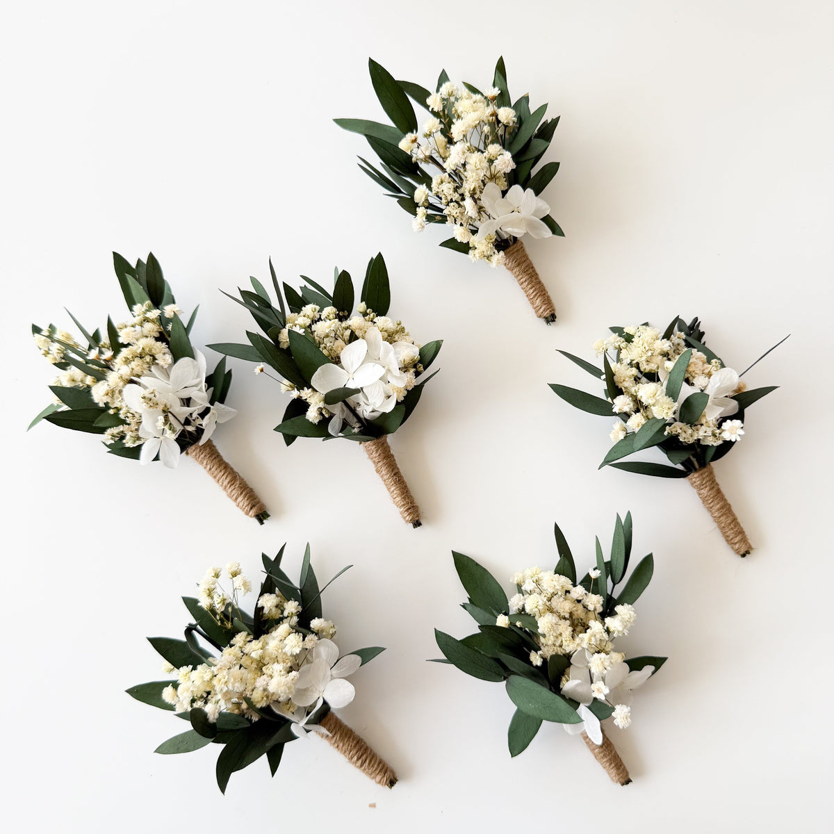 Flat lay display of five dried eucalyptus boutonnieres for groomsmen and groom.