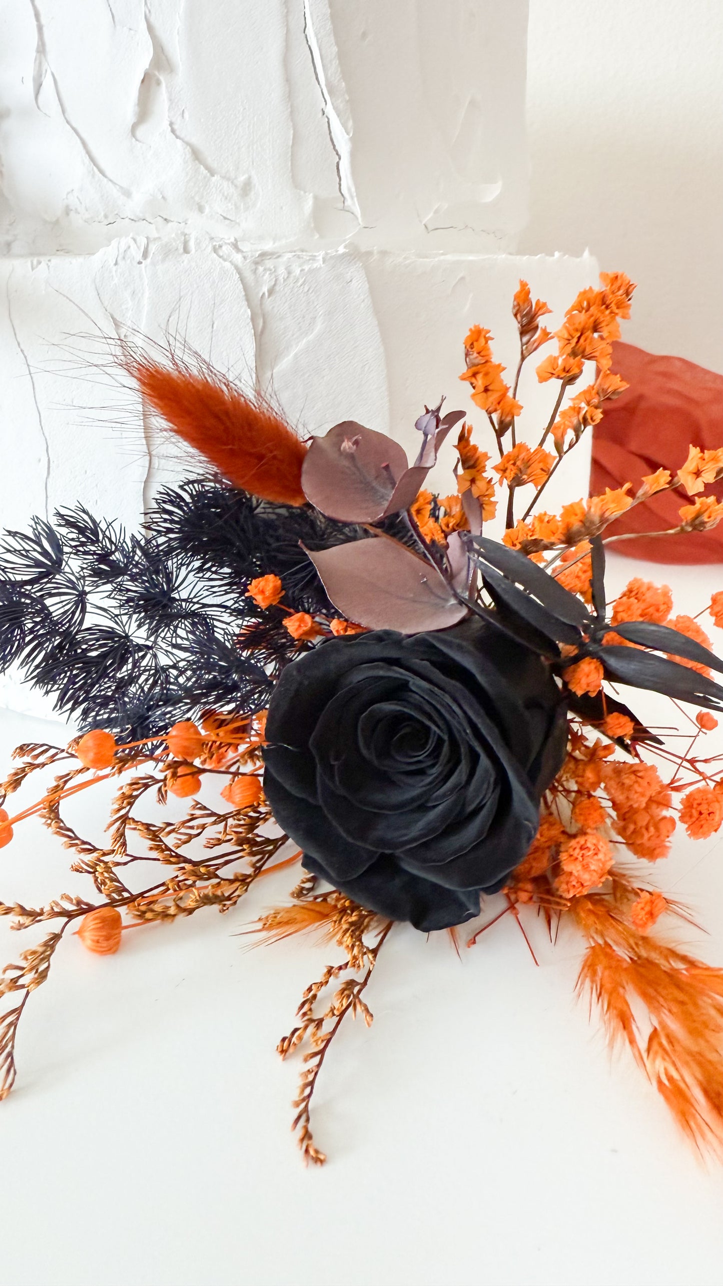 Halloween-inspired wedding cake topper with black rose, burnt orange blooms and preserved foliage