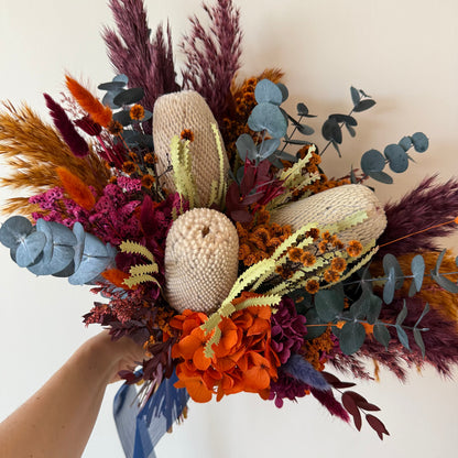 Hand-held Australian native wedding bouquet with dried banksia, orange flowers, eucalyptus and rich burgundy foliage.