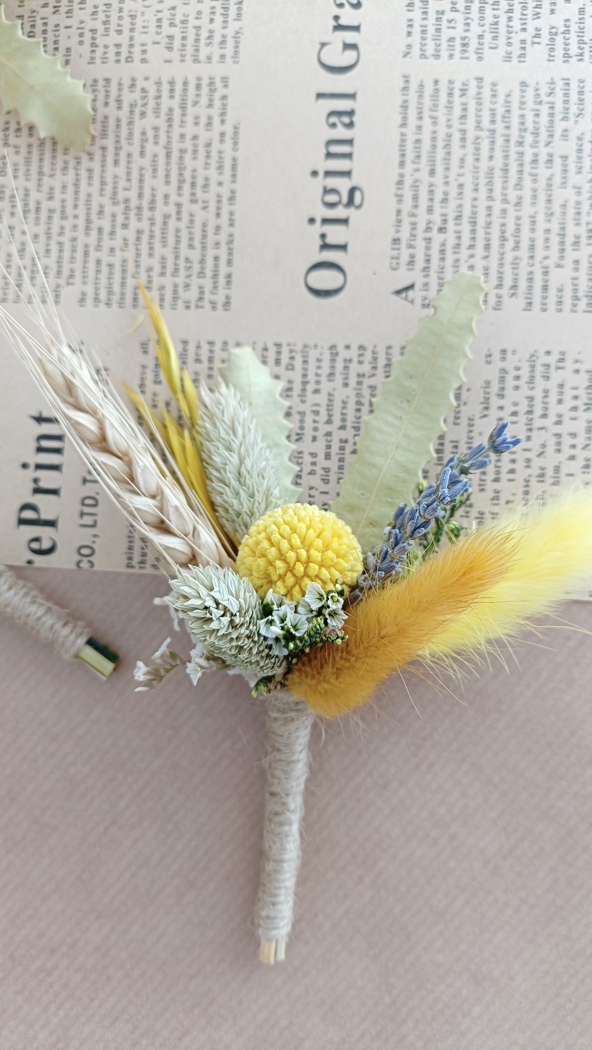  handcrafted boutonnières featuring yellow billy buttons, fluffy bunny tails, dried lavender, and greenery – styled on vintage newspaper background.