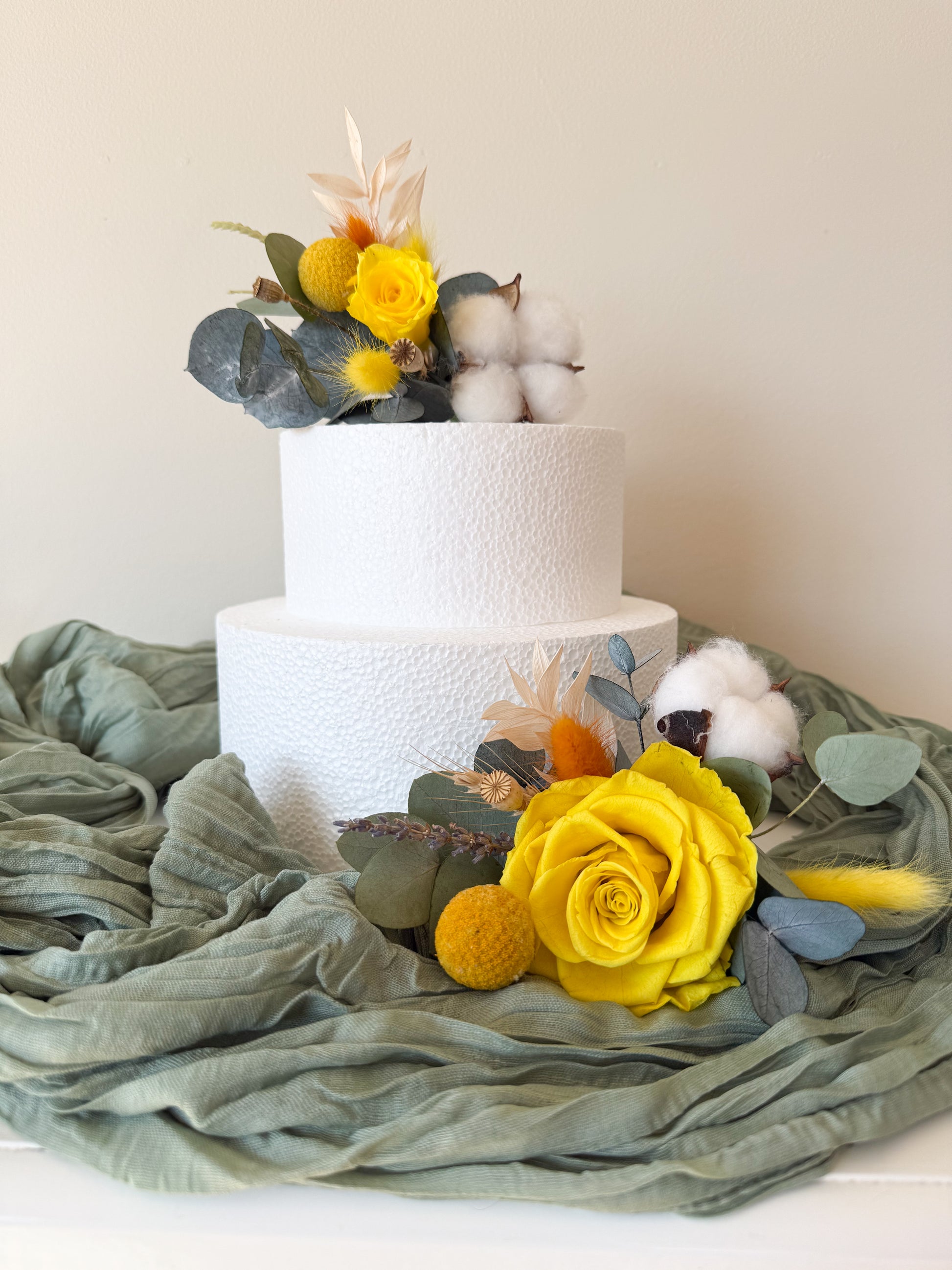Two-tiered white wedding cake with yellow flowers and greenery on a light background
