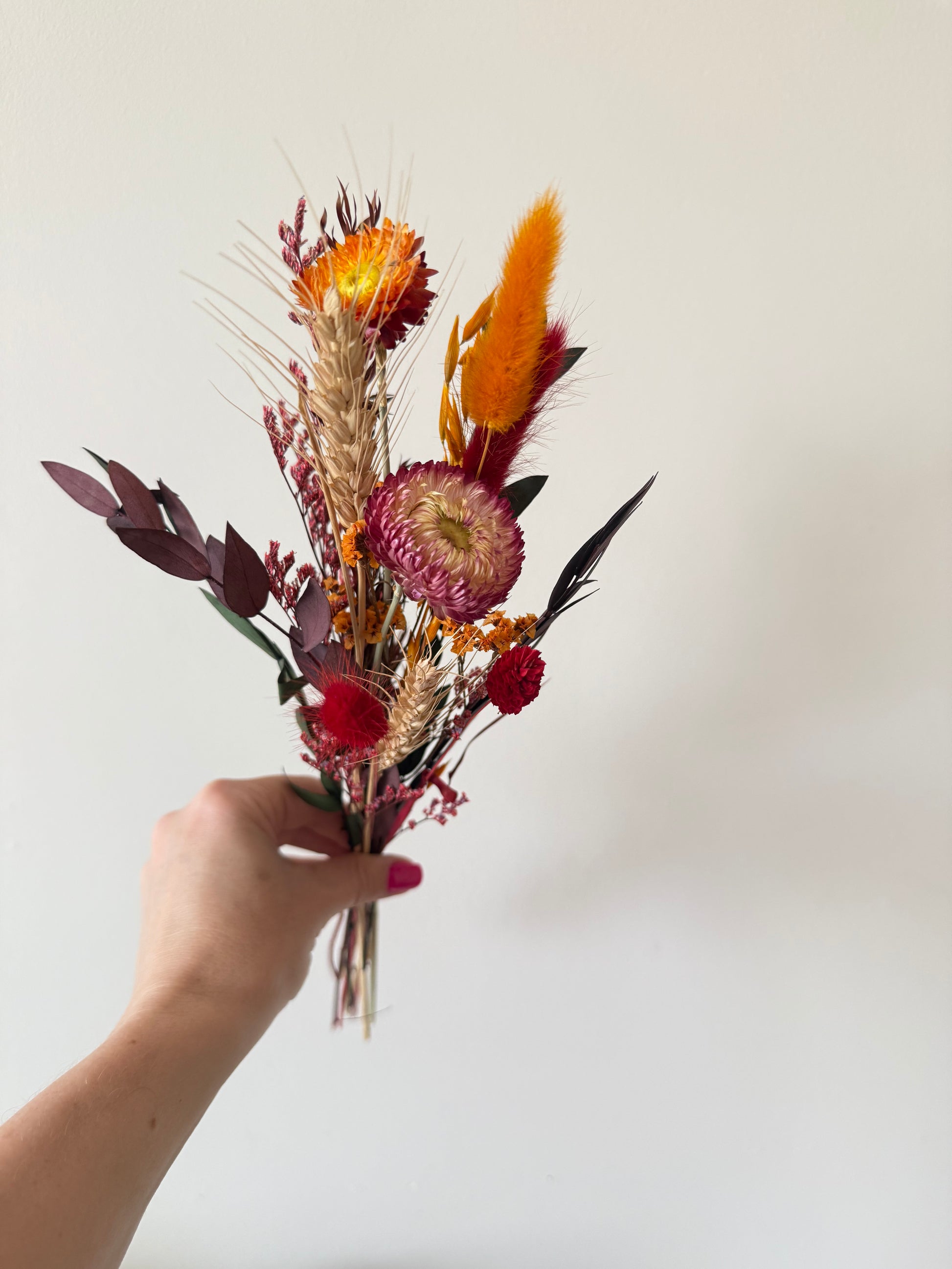 Handmade dried flower arrangement with red and orange bunny tails, strawflowers, and eucalyptus for boho home or wedding decor.