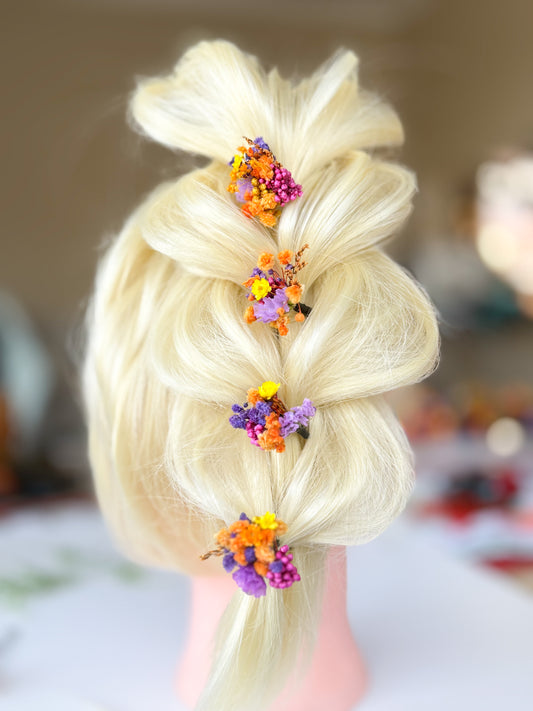 Mannequin head with blonde hair styled in a braid adorned with colorful flowers on a blurred background.