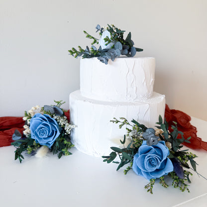 Two-tier white wedding cake decorated with blue roses, dried flowers and preserved greenery, perfect for elegant Australian wedding cakes