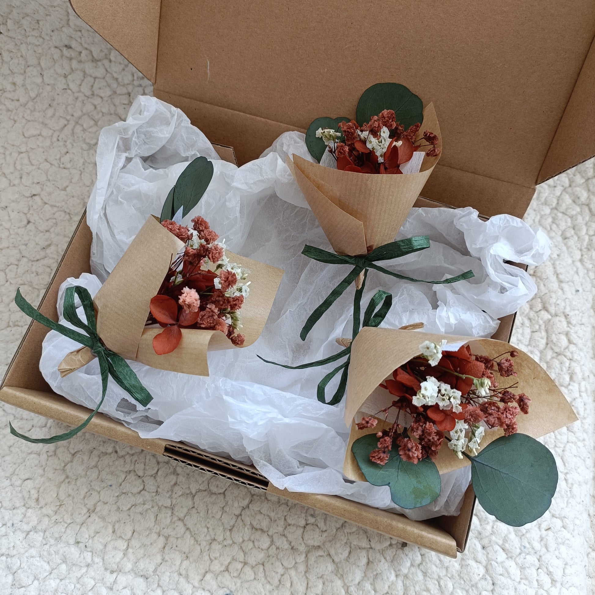 Set of two mini dried flower bouquets in a box, decorated with eucalyptus stems and green ribbon. Each bouquet is crafted with terracotta strawflowers, babyâ€™s breath, and wrapped in kraft paper. Perfectly packaged for wedding favours, thank-you gifts, or bridesmaid proposals with a natural and sustainable touch.