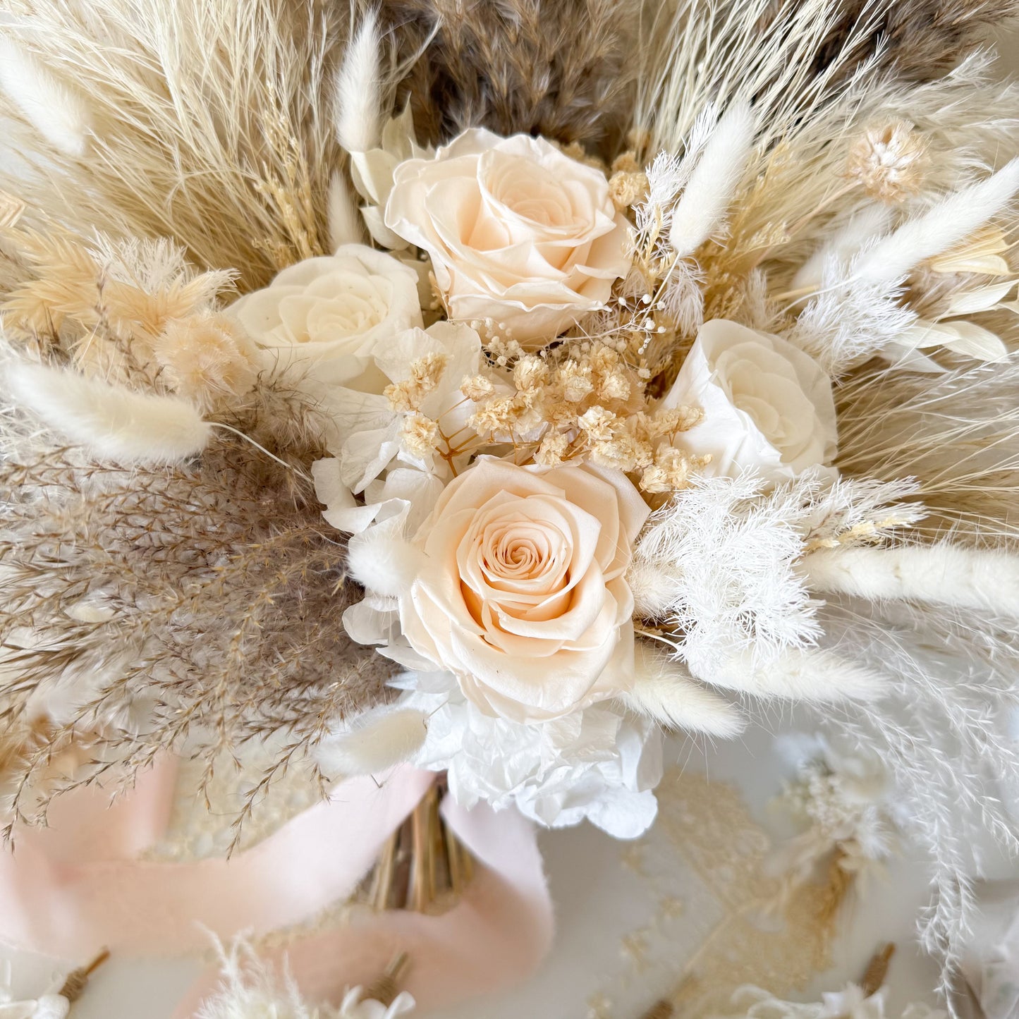 Dried bridal Bouquet of beige roses and dried pampas grass held by a hand.
