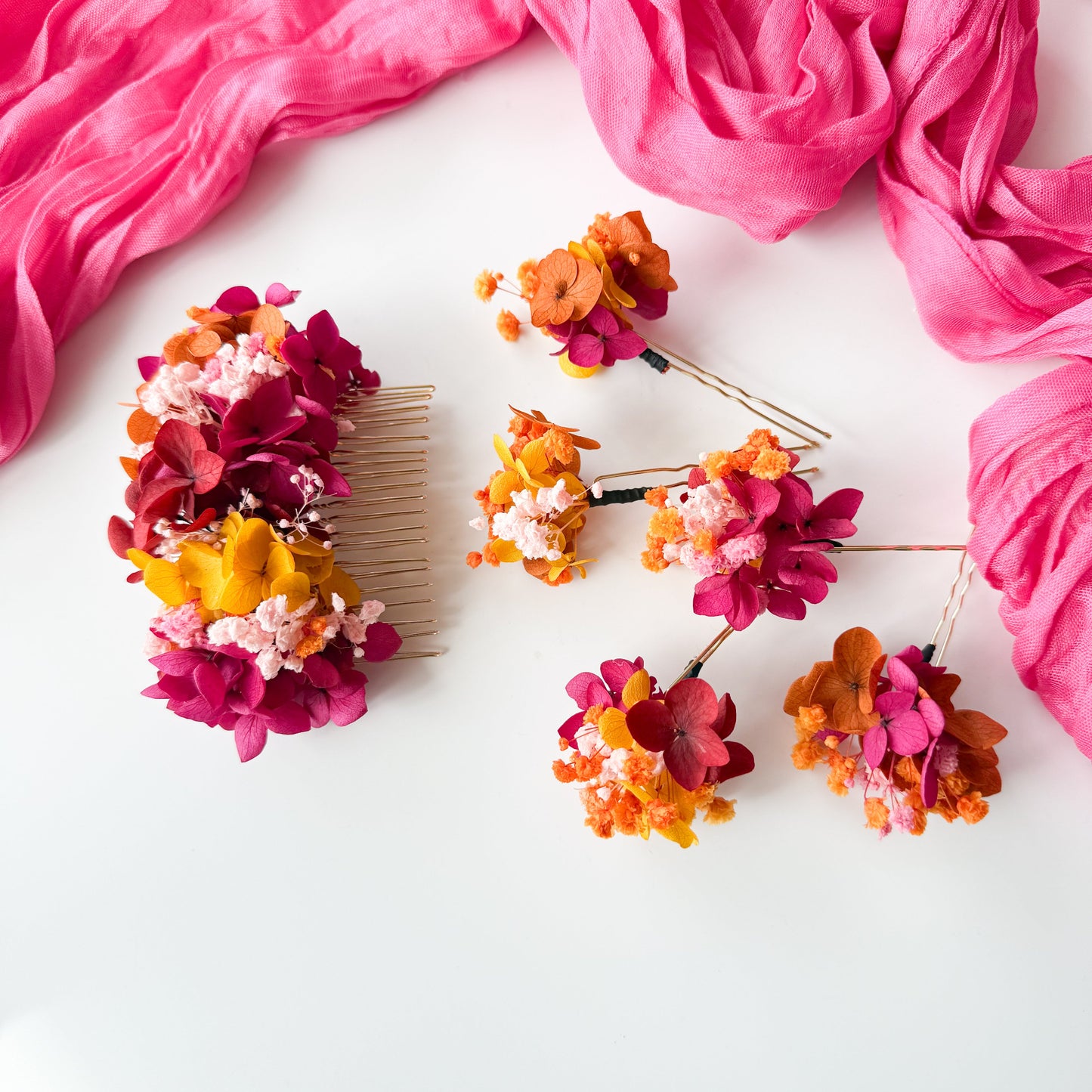 Colorful floral hair accessories on a white background with pink fabric.