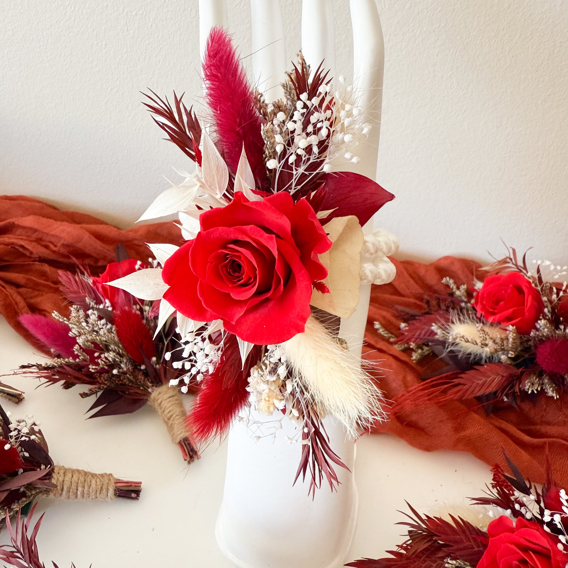 burgundy wrist corsage with red roses and feathers on a white background
