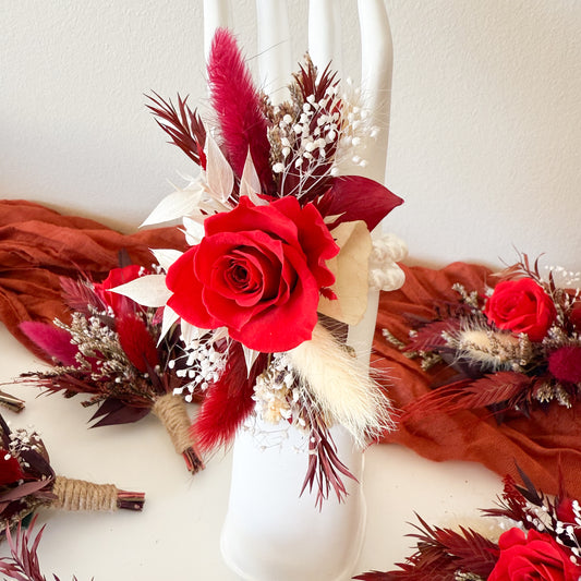 burgundy wrist corsage with red roses and feathers on a white background