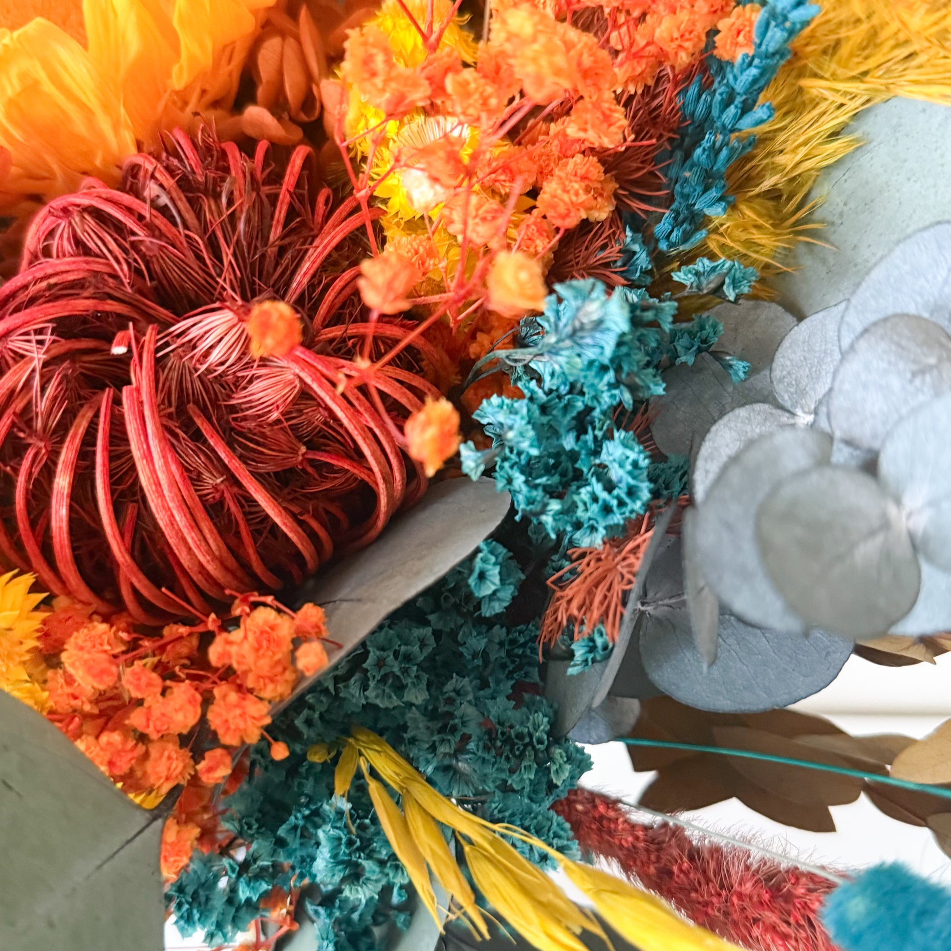 Colorful dried flower arrangement with a wooden base on a neutral background