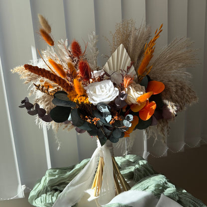 Rustic bridal bouquet featuring pampas grass, dried foliage, sola wood flowers, and bright terracotta accents — handmade boho bouquet for weddings.