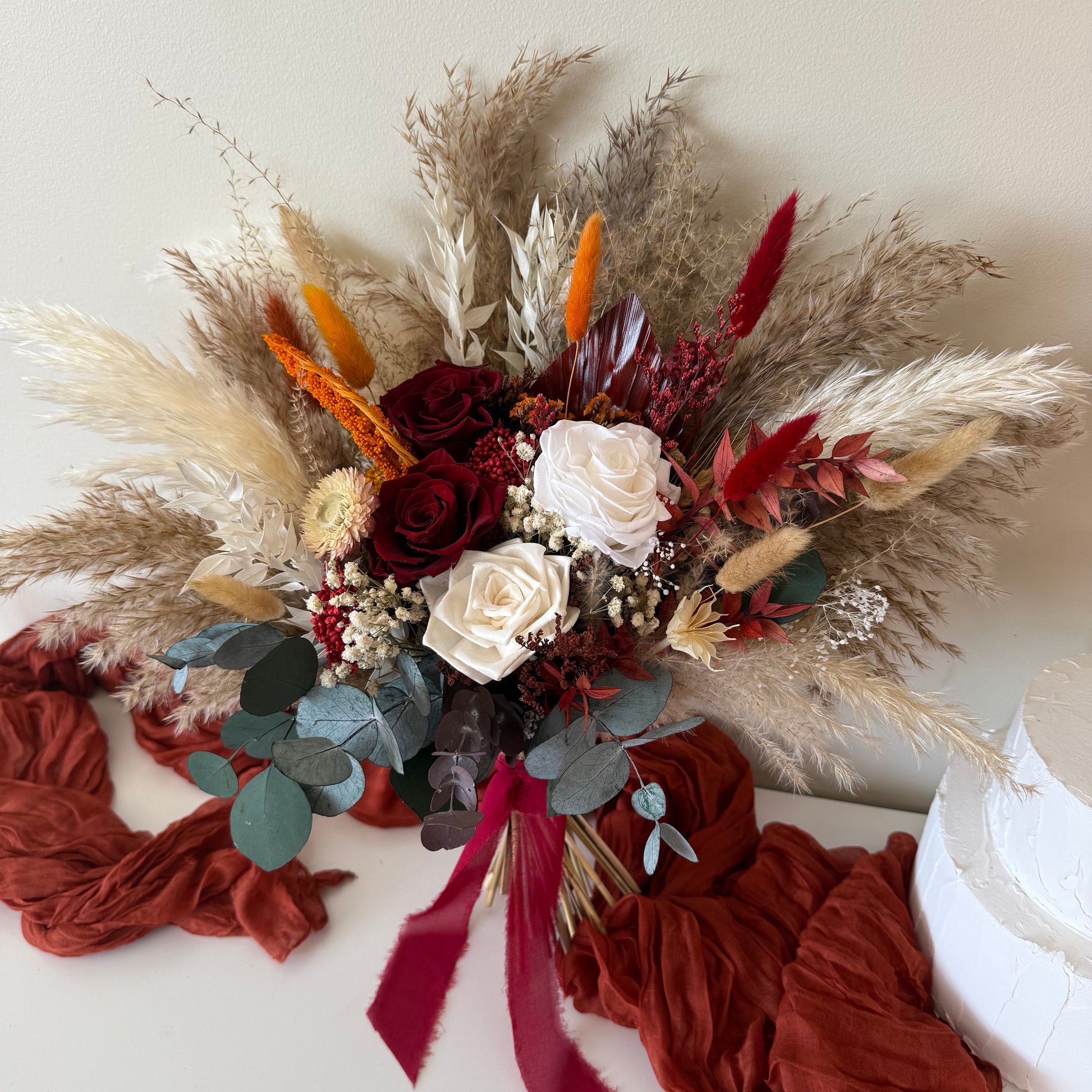 Overhead, angled view of the full dimension of the signature dried wedding bouquet, emphasising the on-trend pampas grass plumes and rich, warm autumn colour palette.