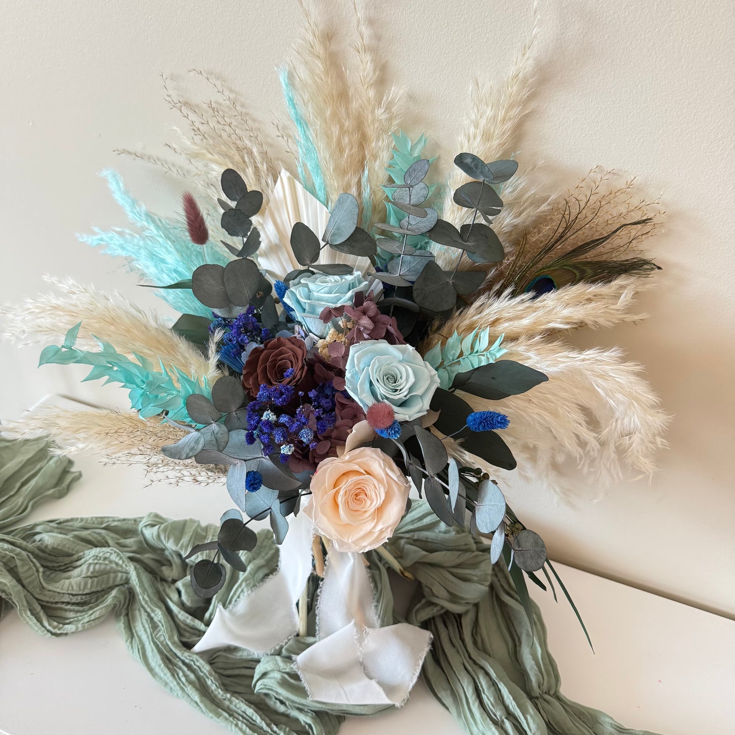 Rustic dried wedding bouquet featuring teal foliage, navy blooms and preserved grass tied with white silk ribbon.