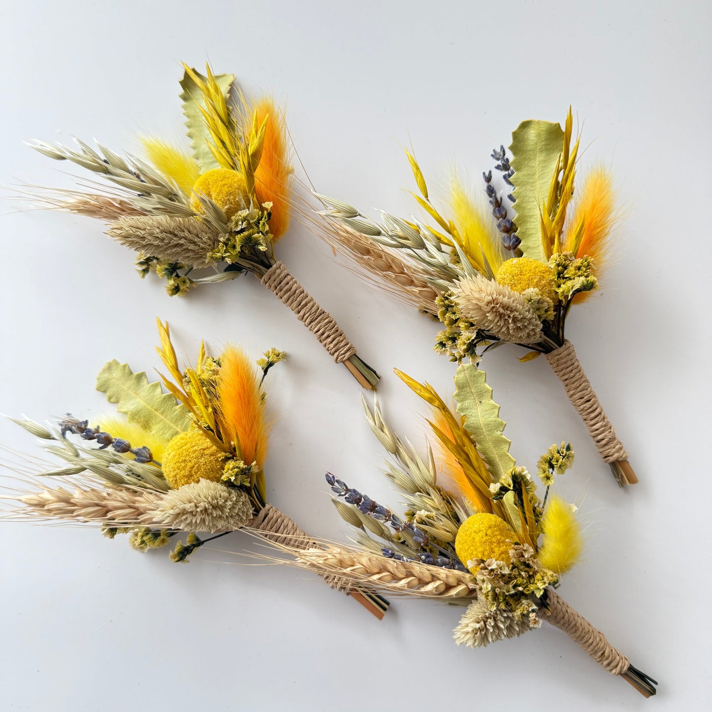 Four dried flower boutonnieres with yellow and orange flowers on a white background