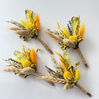 Four dried flower boutonnieres with yellow and orange flowers on a white background