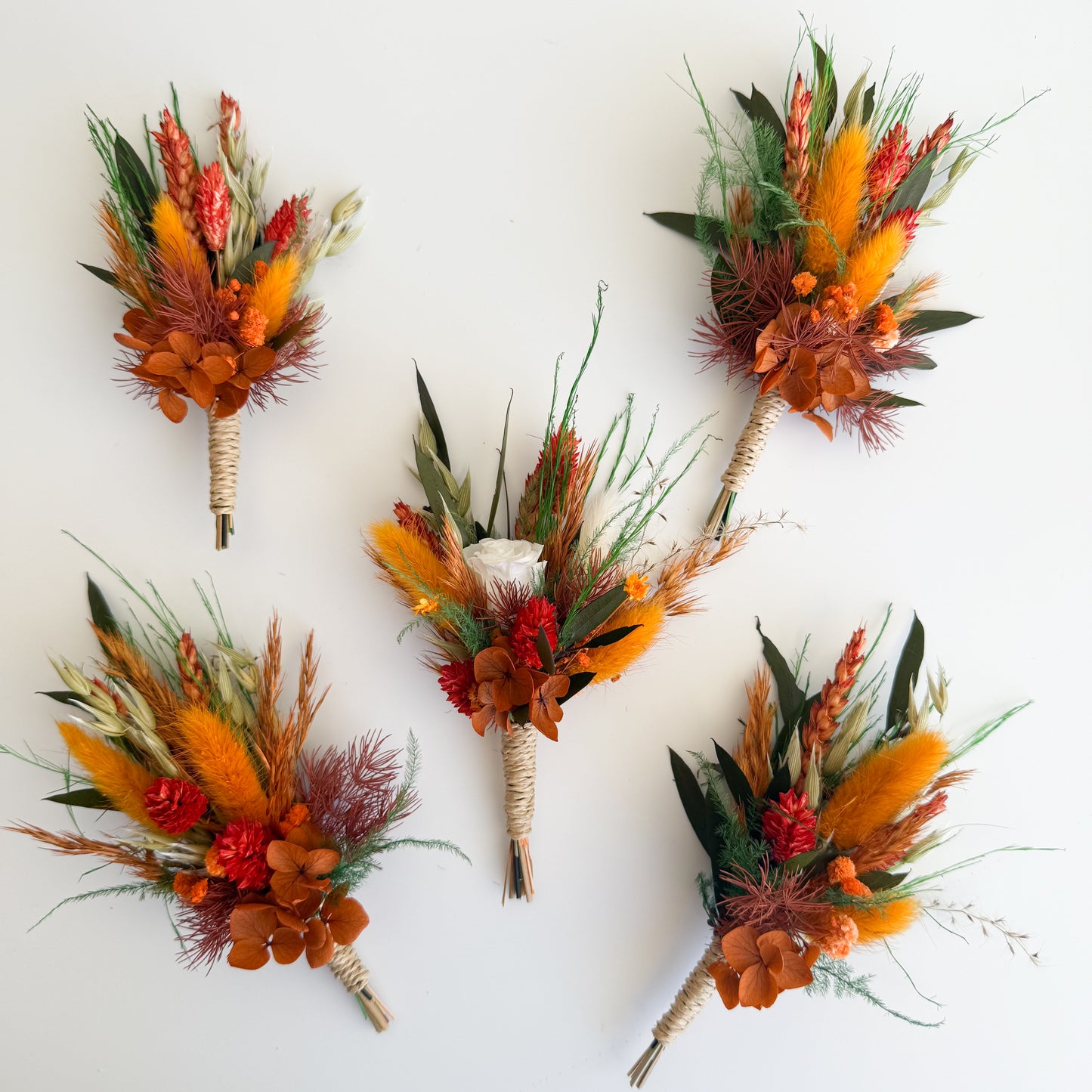 Five autumn-themed boutonnieres with orange, red, and green flowers on a white background.