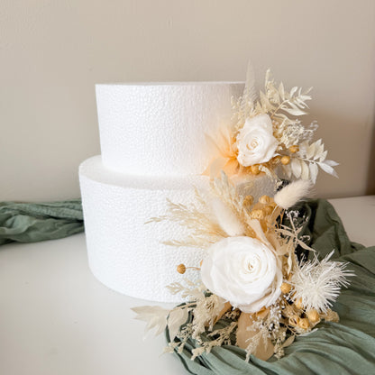 Two-tiered white wedding cake with floral decorations on a light green fabric background.