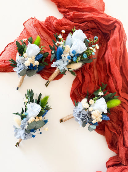 Four floral boutonnieres on a white surface with red fabric in the background