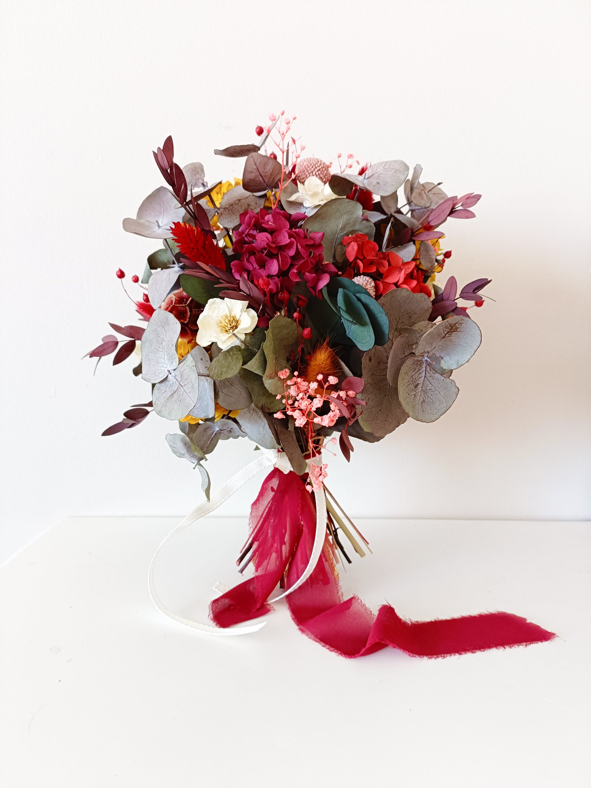 Side view of a dried flower bouquet with preserved rose, hydrangea, ruscus, and eucalyptus in burgundy and mustard tones.