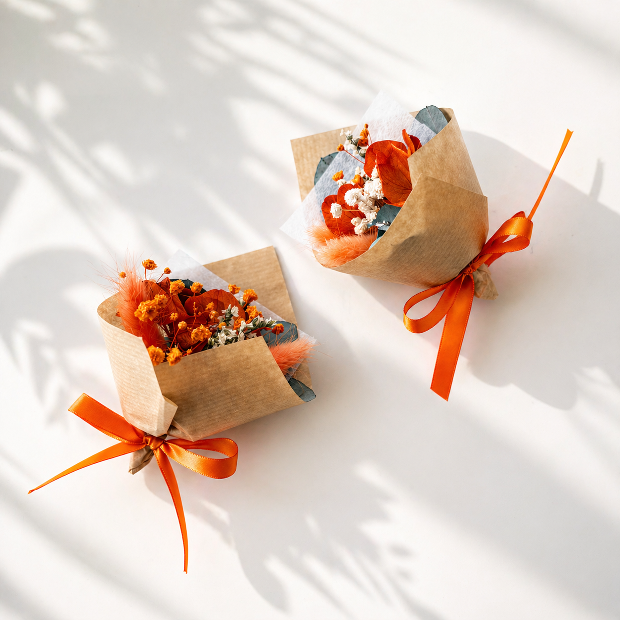 Two small floral arrangements in brown paper packages with orange ribbons on a light background