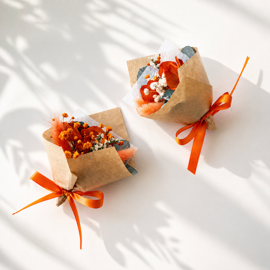 Two small floral arrangements in brown paper packages with orange ribbons on a light background