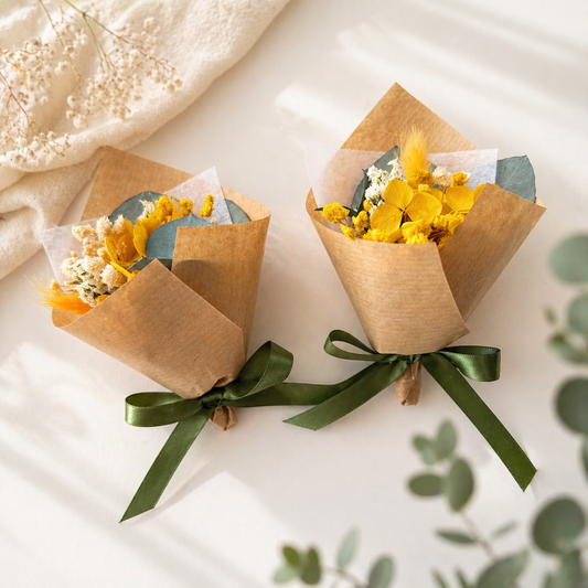 Two small flower bouquets wrapped in brown paper with green ribbons on a light background.