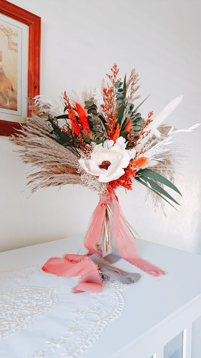 Close-up of a sola wood flower in an ivory dried bouquet, surrounded by preserved leaves and burnt orange details.
