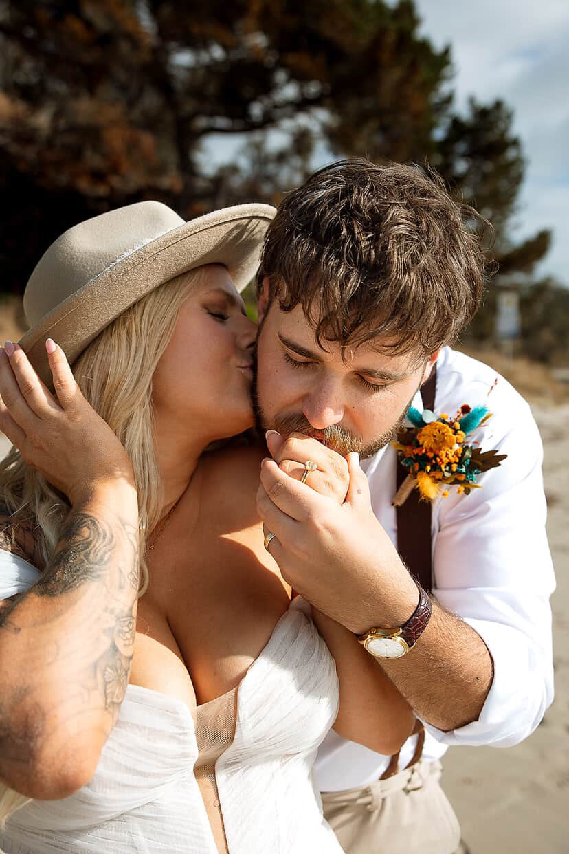 Bride and groom embracing on the beach with sunflower and teal dried flower wedding bouquet and boutonniere