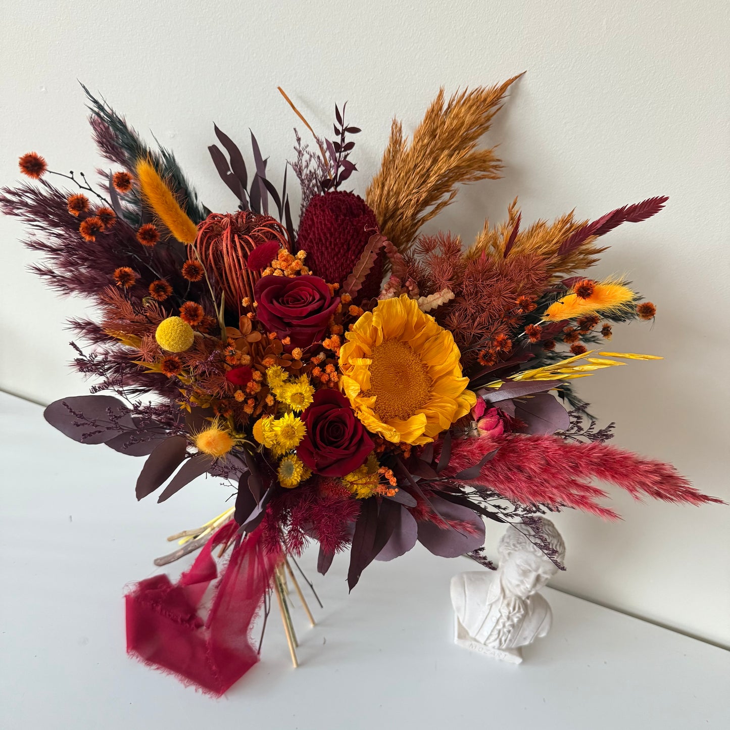 Autumnal flower arrangement with red, yellow, and brown colors on a white surface.
