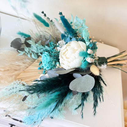 Decorative floral arrangement with teal, white, and green flowers on a textured surface.