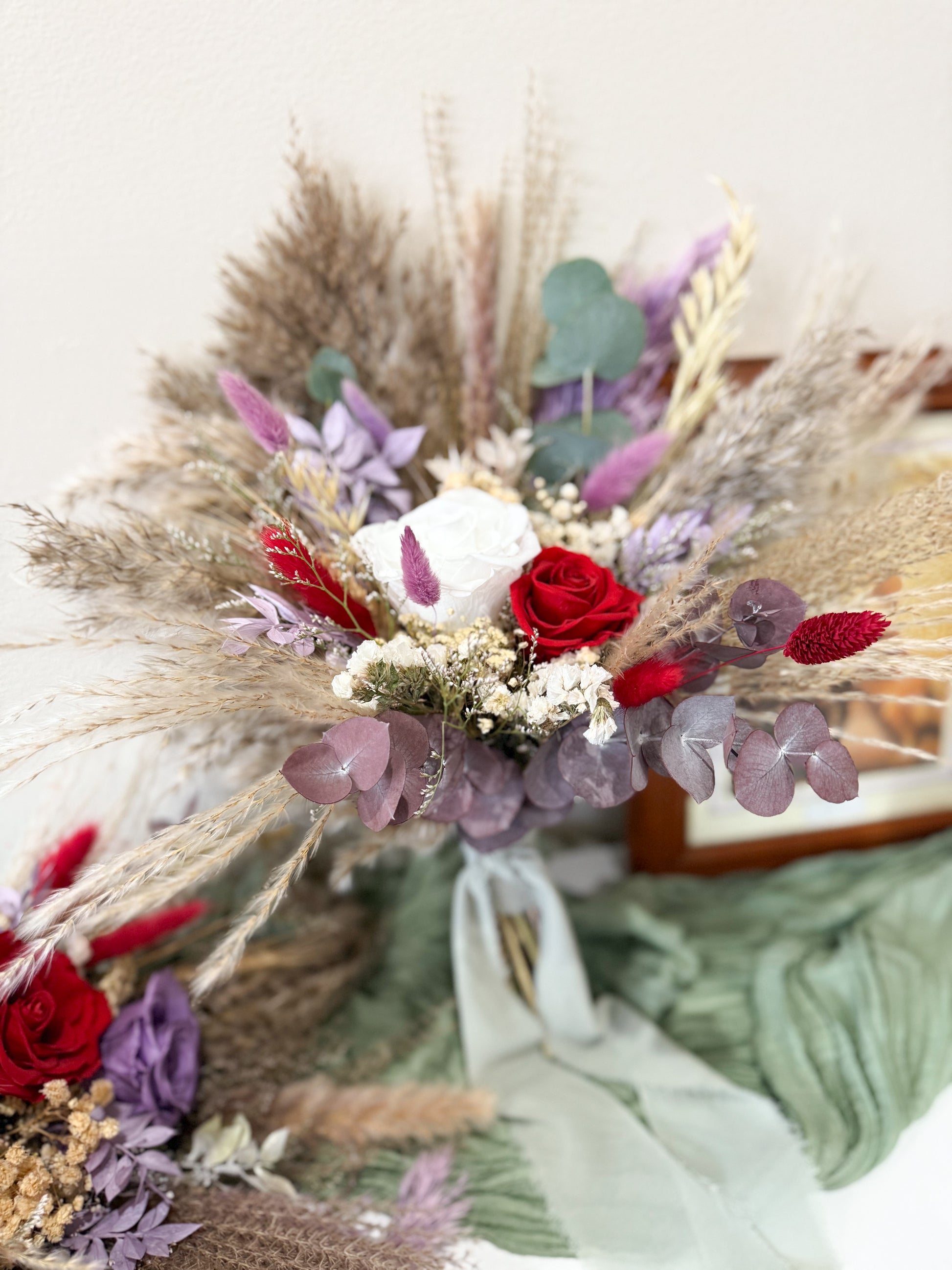 Decorative floral bridal flowers with dried grasses, red roses, and purple flowers on a white background.