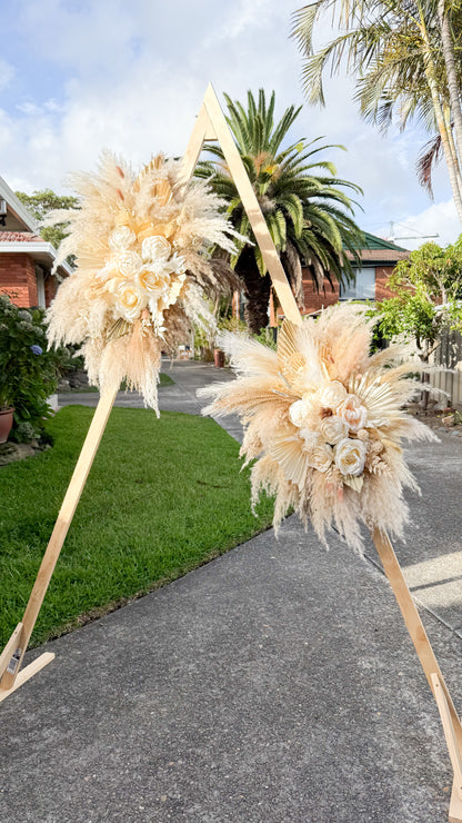 Boho wedding arch flowers with pampas grass, dried palms, and ivory sola peonies and roses arranged on a wooden arch outdoors
