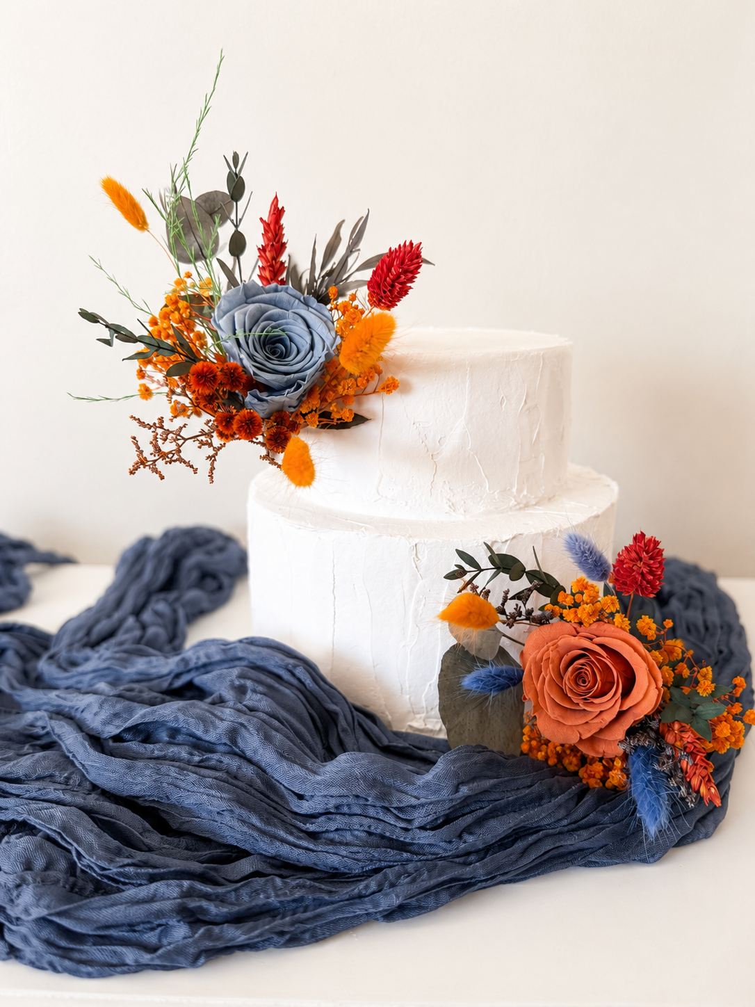 Handmade wedding cake floral decorations in blue and amber tones, arranged with dusty blue roses, amber blooms and autumn foliage.