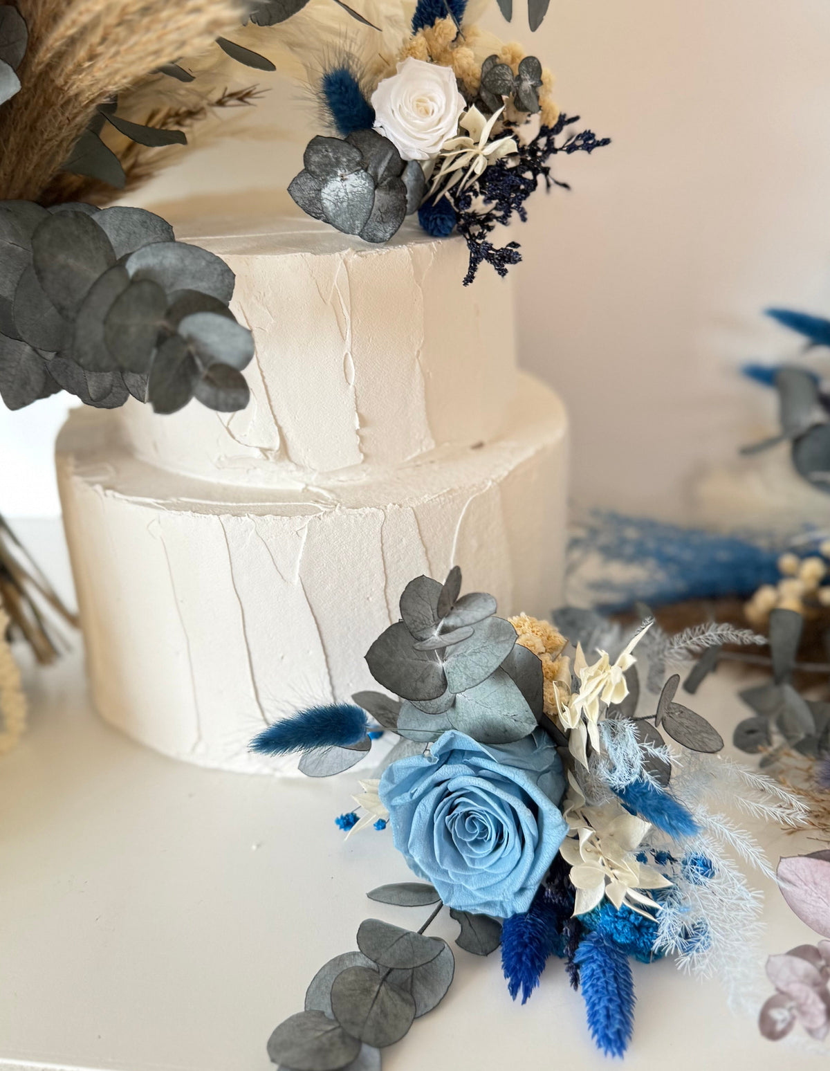 Handmade wedding cake floral decorations in blue sky and ivory tones, arranged with soft blue roses, ivory flowers and natural preserved greenery.