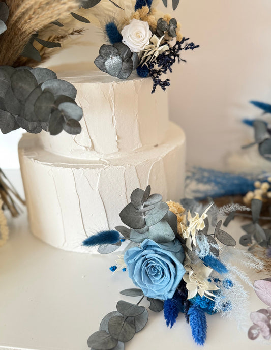 Handmade wedding cake floral decorations in blue sky and ivory tones, arranged with soft blue roses, ivory flowers and natural preserved greenery.