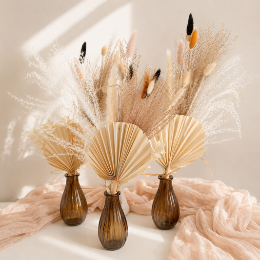 Three brown vases with dried pampas grass and feathers on a light background