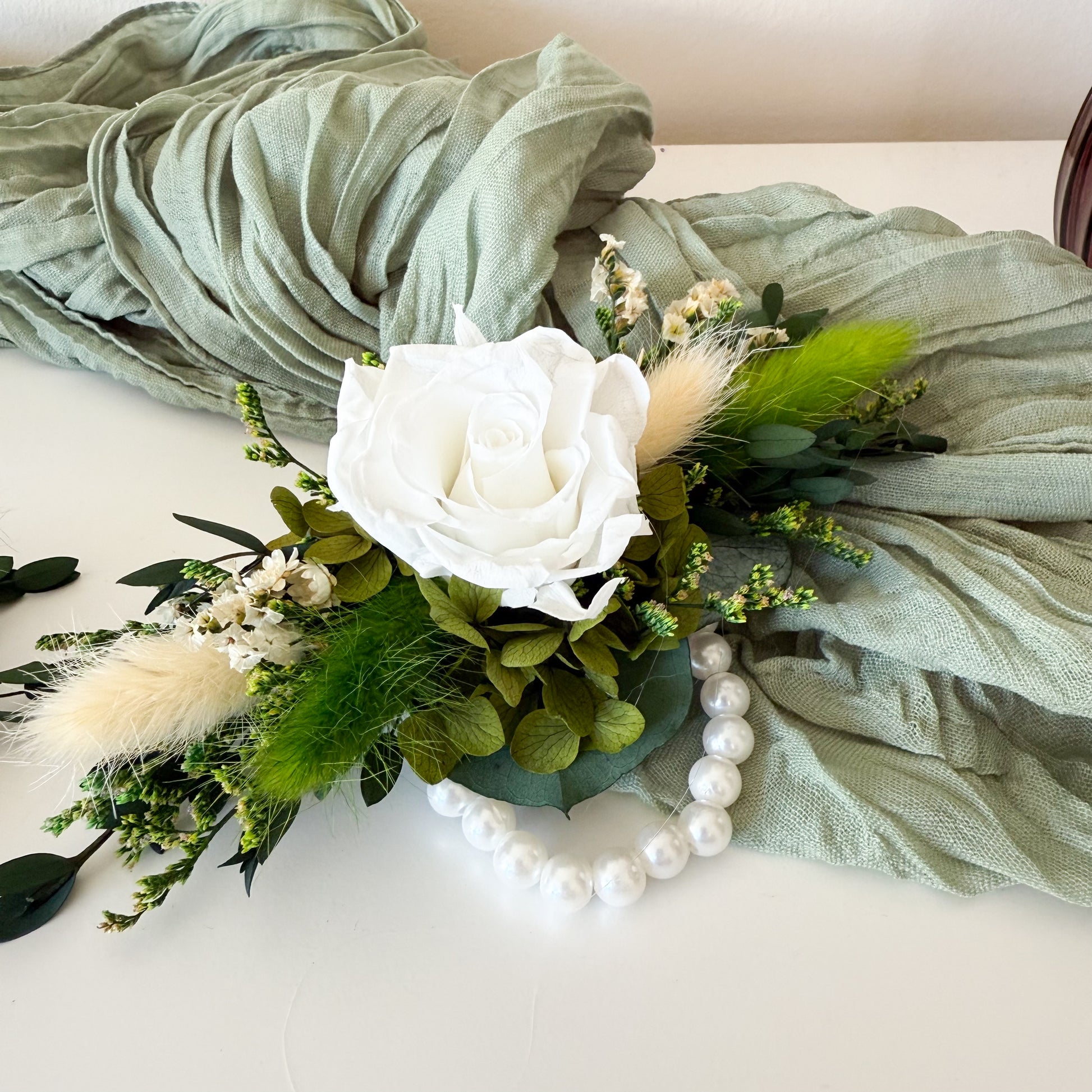 dried Floral arrangement with a white rose, greenery, and pearls on a light background