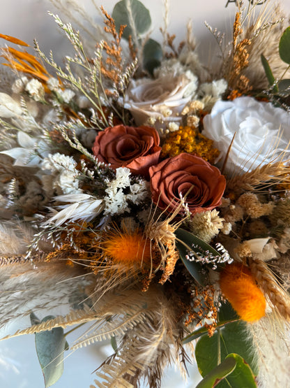 Dried floral arrangement with roses, feathers, and other elements on a light background