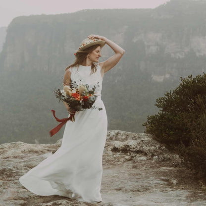 Woman in a white dress with a bouquet standing on a mountainous landscape